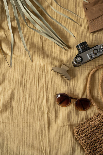 Set de voyage : chapeau panama, appareil photo rétro hipster, sac à provisions en paille, lunettes de soleil, feuille de palmier tropical sur toile de couverture en mousseline jaune. Esthétique bohème plat composition laïque pour les médias sociaux, blog - Photo, image