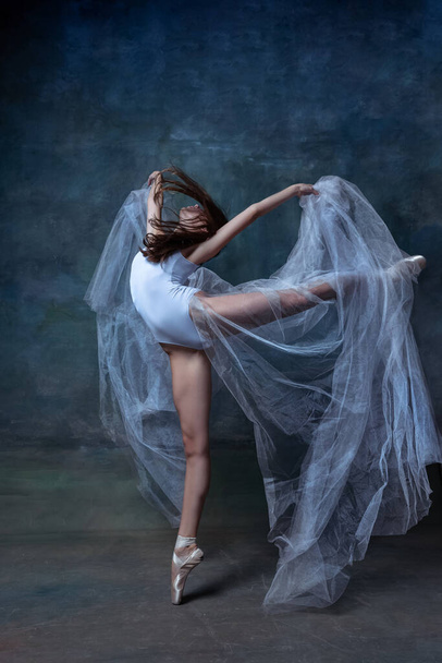 Young ballerina in pointe shoes and with white cloth, scarf dancing isolated on dark vintage studio background. Art, motion, action concept. - Foto, imagen