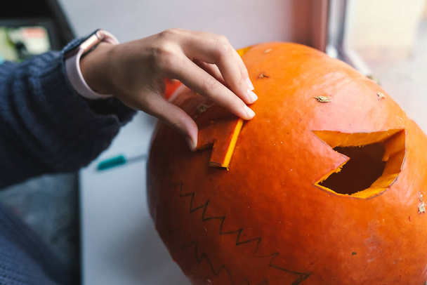 Hand of a young woman cutting out a Halloween pumpkin - Фото, изображение