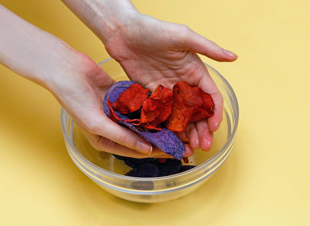 Female hands holding colorful vegetable chips over transparent glass bowl - Photo, Image