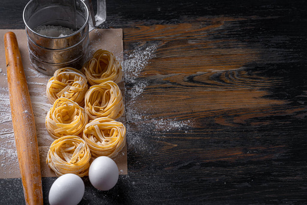 Zelfgemaakte fettuccine pasta gevouwen in de vorm van een nest. Thuis koken met ingrediënten voor zelfgemaakte traditionele Italiaanse fettuccine pasta. - Foto, afbeelding