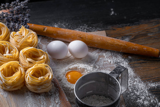 Homemade fettuccine pasta folded in the shape of a nest. Home cooking with ingredients for homemade traditional Italian fettuccine pasta. - Foto, afbeelding
