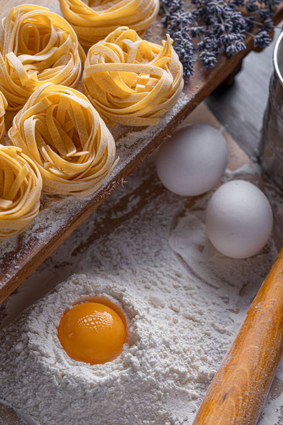 Homemade fettuccine pasta folded in the shape of a nest. Home cooking with ingredients for homemade traditional Italian fettuccine pasta. - Zdjęcie, obraz