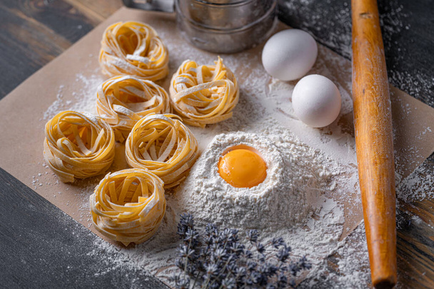 Homemade fettuccine pasta folded in the shape of a nest. Home cooking with ingredients for homemade traditional Italian fettuccine pasta. - Foto, afbeelding