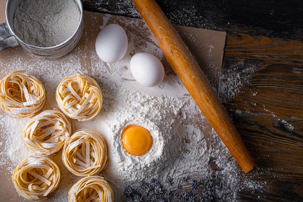 Homemade fettuccine pasta folded in the shape of a nest. Home cooking with ingredients for homemade traditional Italian fettuccine pasta. - Foto, Bild