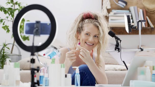 Blonde sorrindo mulher influenciador blogueiro gravando um vídeo tutorial na câmera do smartphone mostrando batom. Feminino vlogger fazendo um vlog de beleza para produtos de maquiagem seu canal de internet on-line. - Foto, Imagem