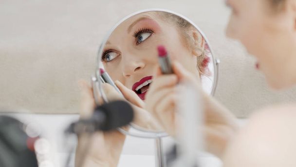 Usmívající se blondýnka vlivný blogger nahrávání video tutorial, natočené zblízka v zrcadle, ukazuje, jak aplikovat kosmetiku na rty make-up. Žena vlogger dělat krásu vlog pro její online internetový kanál. - Fotografie, Obrázek