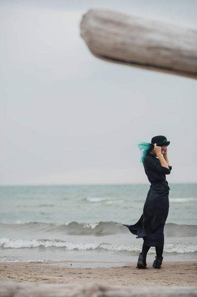 beautiful woman with blue hair and hat walks on the windy beach - Fotoğraf, Görsel