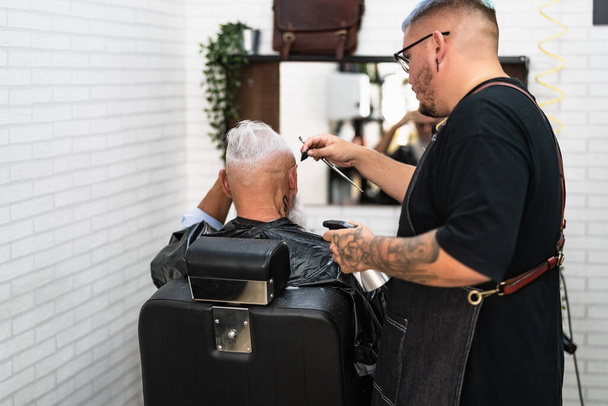 Cabeleireiro masculino corte de cabelo para barba cliente sênior - Cabeleireiro jovem que trabalha na barbearia - Cuidados de saúde e corte de cabelo conceito salão - Foto, Imagem