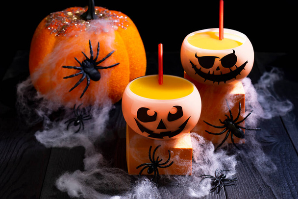 Halloween koktajl z dyni w okrągłych szklankach ze strasznymi kagańcami. Tradycyjne napoje dyniowe, dynia, pajęczyny i pająki na Halloween party - Zdjęcie, obraz
