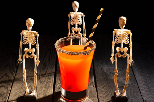Halloween red cocktail Bloody Mary surrounded by skeletons. Scary drinks with decorations for Halloween party - Photo, Image