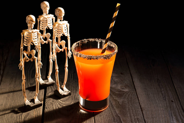 Красный коктейль на Хэллоуин Кровавая Мэри в окружении скелетов. Страшные напитки с украшениями для Хэллоуина - Фото, изображение