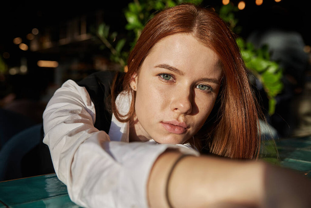 young redhead pretty girl with long hair lays her head on her arms and table - Photo, Image