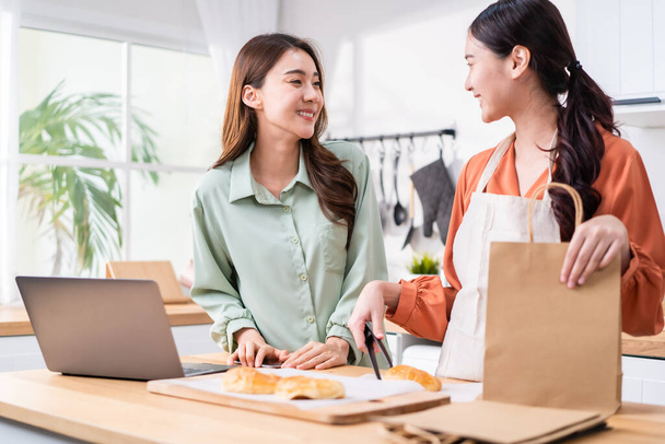 Asian beautiful business woman and friend bake bakery and sale in house. Attractive lesbian couple feel happy and exciting for success in entrepreneur sell food order from home then high five together - Photo, Image