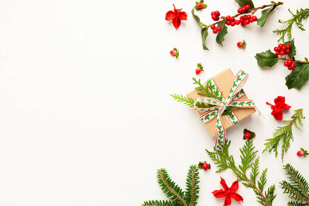 Christmas background with gift box, branches of fir tree, evergreens and holly with red berries on white. Winter festive nature concept. Flat lay, copy space. - Photo, image