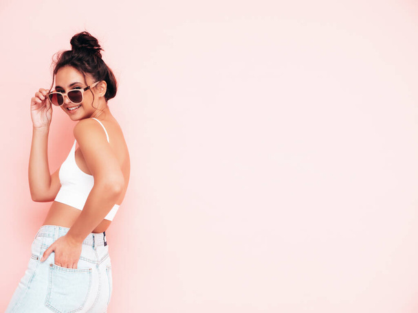 Young beautiful smiling female in trendy summer clothes. Sexy carefree woman posing near pink wall in studio. Positive brunette model having fun and going crazy. Cheerful and happy in sunglasses - Φωτογραφία, εικόνα