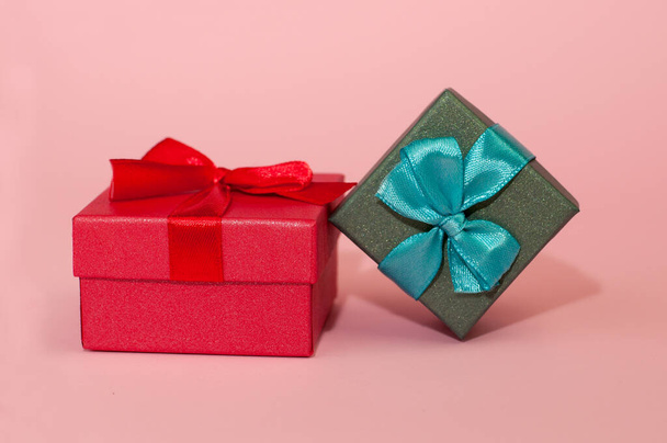A red box with a red ribbon and a green box with a blue bow on a pink background - Фото, зображення