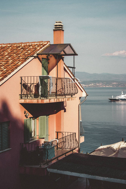 Pink residential house with balconies bounded by a metal structure. In the background a yacht and Croatian mountains. - Fotó, kép