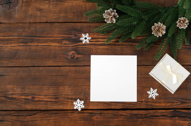 Blank square paper mockup gift box on wooden vintage table background. Flat lay, top view, copy space, minimalist. Christmas and New Year concept. Fir wreath - Photo, Image