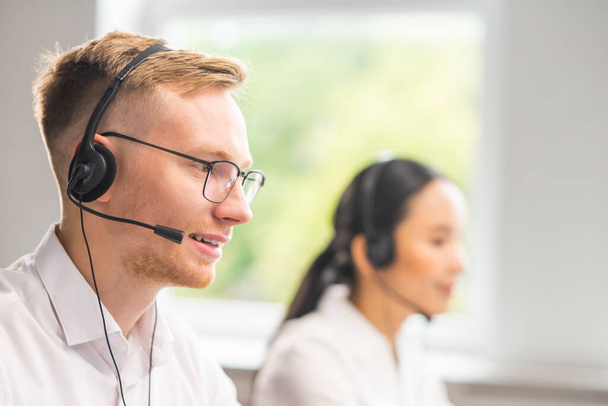 Diverse team of young professionals is working in the phone support office. Working day of sales managers in the call center. Business, telephone consulting and problem solving. - 写真・画像