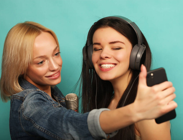 lifestyle, emotion and people concept: Happy young girls with microphone take picture with smartphone over blue background - Фото, изображение