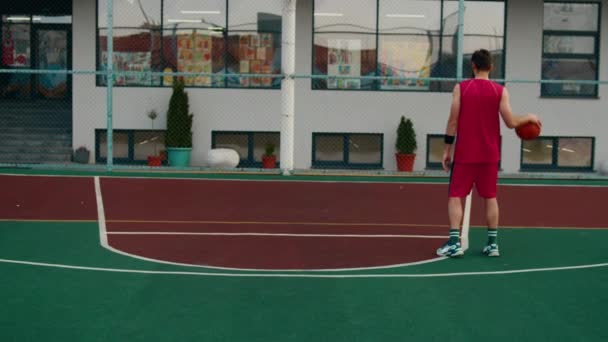A modern stadionban a kosárlabdázó fiatalember bedobja a labdát a kosárba, piros sportruhát visel. - Felvétel, videó