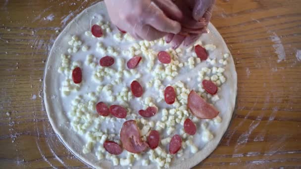 Μαγείρεμα πίτσα διαδικασία. Γυναικεία χέρια βάζουν κομμάτια λουκάνικου στην ωμή πίτσα με σαλάμι και τυρί. Λεπτή ιταλική πίτσα με λουκάνικο σε πιτσαρία. - Πλάνα, βίντεο