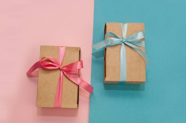 two craft gift boxes tied with pink and blue satin ribbons on pink and blue backgrounds - Foto, Bild