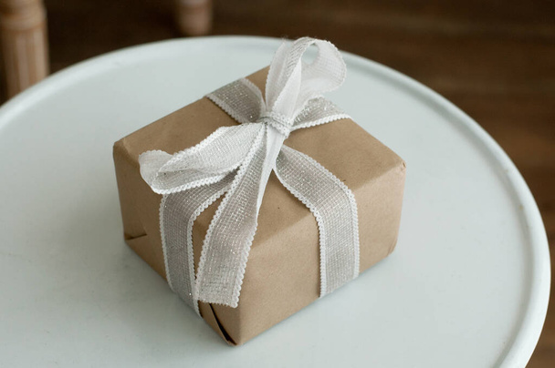 a box wrapped in craft paper, untidily tied with a white ribbon with a bow on a white background - Fotó, kép