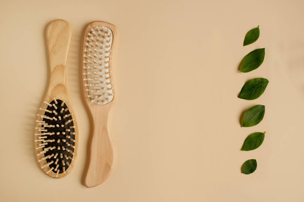 zwei Massagekämme aus Holz und grüne Blätter in Form einer senkrechten Reihe auf beigem Hintergrund mit Platz für Text - Foto, Bild