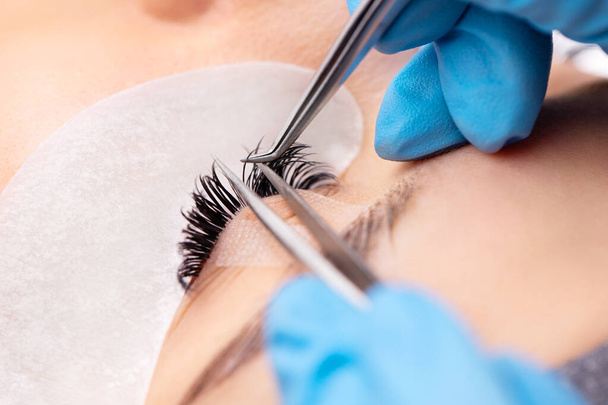 Eyelash extension procedure. The working process of professional beauty master lengthening female lashes. Fake eyelashes. Eyelashes extensions close up. Makeup artist and client in beauty salon. - Photo, Image