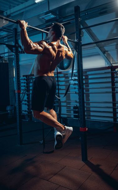Portrait of muscled athlete, bodybuilder workouts alone at sport gym, indoors. Concept of sport, activity, healthy lifestyle - Foto, Imagen