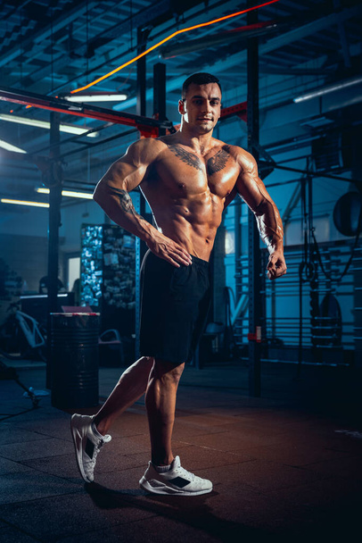 Portrait of young man, muscled athlete, bodybuilder posing at sport gym, indoors. Concept of sport, activity, healthy lifestyle - Photo, Image