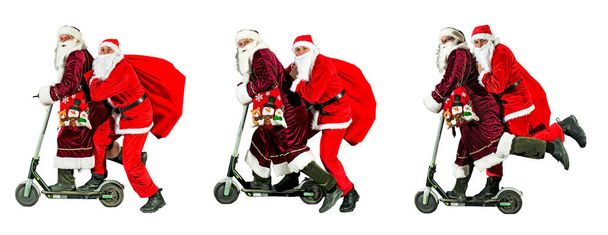 Zwei fröhliche Weihnachtsmänner mit Neujahrsmützen und roten Kostümen fahren auf einem Motorroller mit Geschenktüten. Drei Isolate auf weißem Hintergrund. Frohes neues Jahr 2022. Frohe Weihnachten. Konzept. - Foto, Bild