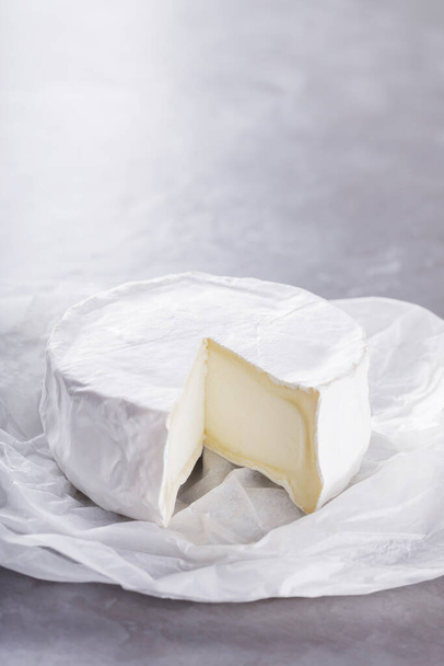 Camembert on a gray cement background. Soft cheese with white mold on parchment paper. Copy space. Top view - Foto, Bild