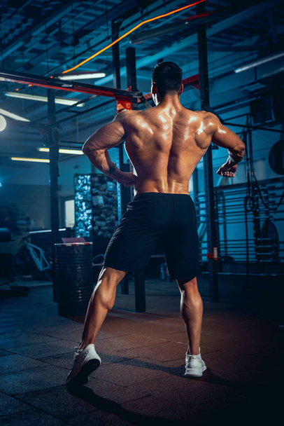 Portrait of young man, muscled athlete, bodybuilder posing at sport gym, indoors. Concept of sport, activity, healthy lifestyle - Fotografie, Obrázek