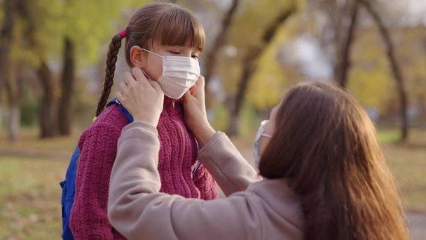 Anne küçük çocuğa tıbbi maske takıyor, Coronavirüs kovid 19 'a karşı koruma, sırt çantası, mutlu aile, modern salgın hayatı, öğrenci sağlığı güvenliği, korona mikrobu, anneye sarılma. - Fotoğraf, Görsel