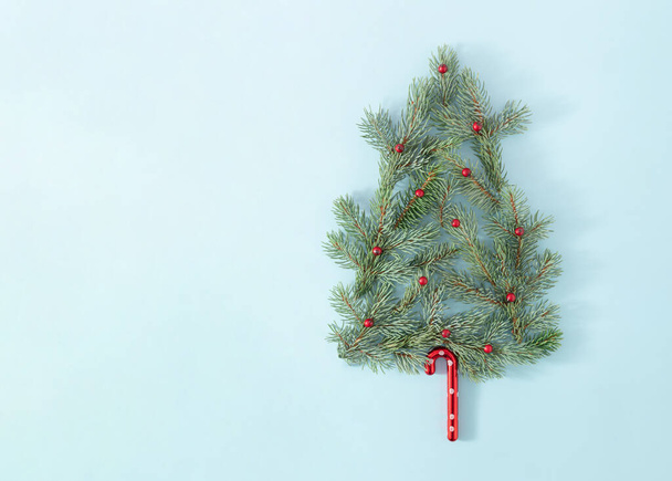 鮮やかな青を背景に赤い果実と装飾が施されたクリスマスツリーの枝。コピースペースと創造的な新年の概念。最小冬の休日フラットレイアウト. - 写真・画像