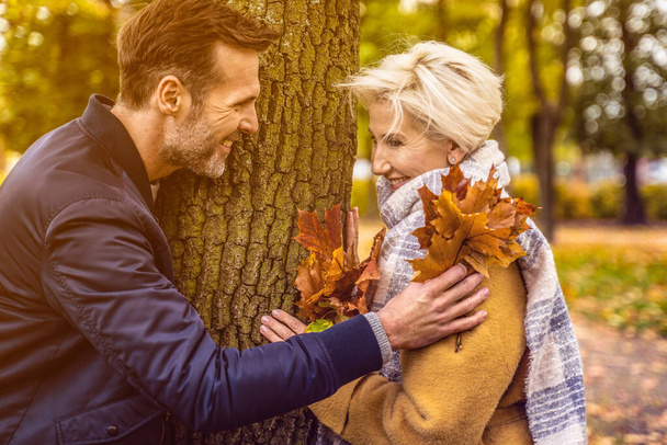 Portrait of an adult couple in love. Handsome man and a beautiful woman having fun together in the sunny park. Autumn toned image - Photo, image