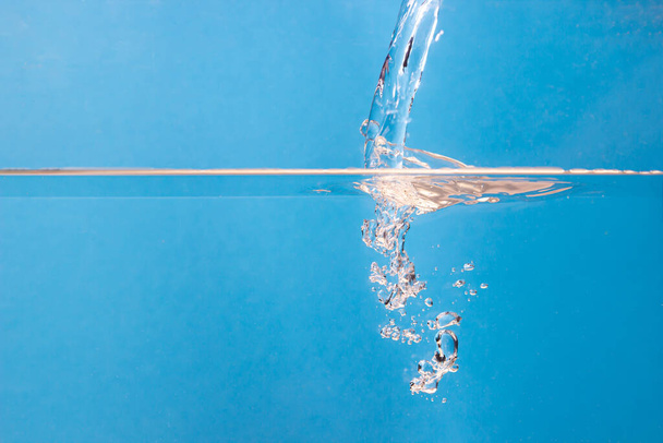 Water pours onto the surface of the water on a blue background. Clean drinking water - Photo, Image