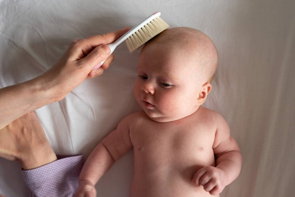 Cepillo y cuidado del bebé. Madre peinando el cabello recién nacido - Foto, imagen