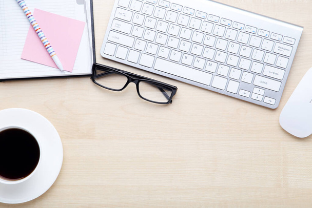 Computer keyboard with notepad, glasses and cup of coffee on wooden table - 写真・画像