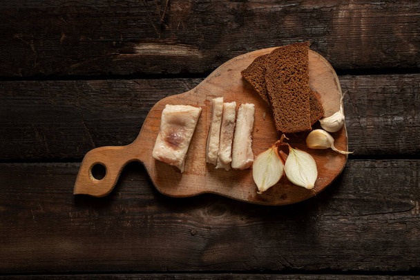 шматок бекону цибуля часник чорний хліб на дерев'яному столі, обід вдома з беконом
 - Фото, зображення