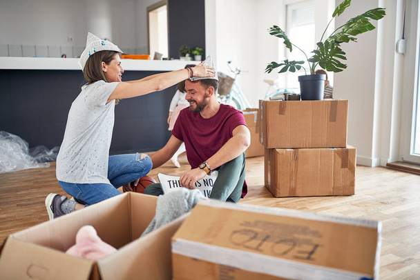 young caucasian couple having fun in brand new apartment, preparing to work and unpack thing, wearing paper hats - Foto, imagen