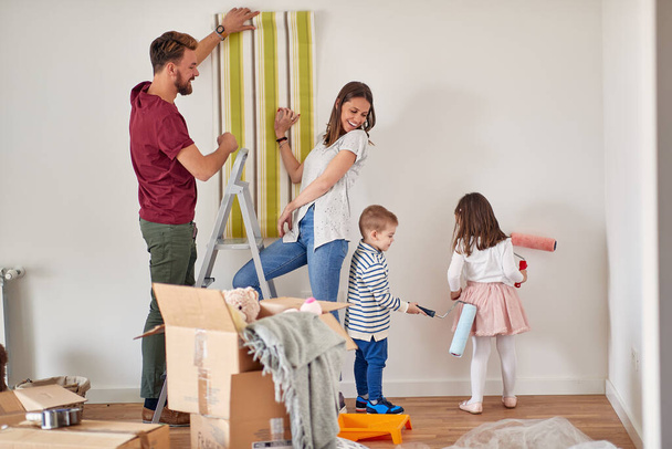A young family in a cheerful atmosphere is painting and decorating their new home they have just moved in. Home, family, moving - Photo, Image