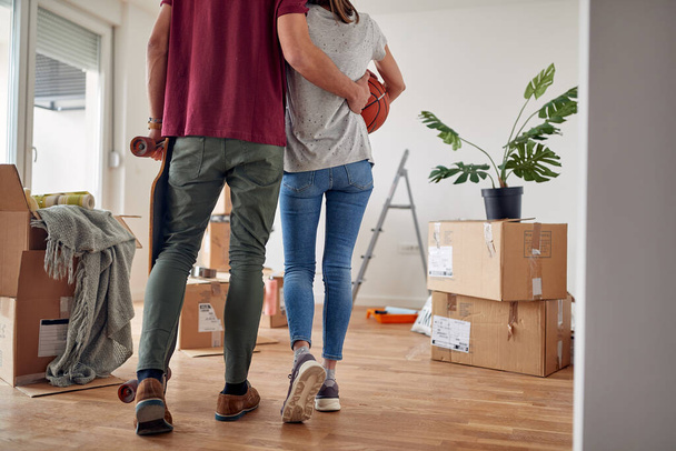 detail, cropped image of young couple from behind holding  each other, walking in new apartment with unpacked boxes around them - Foto, imagen