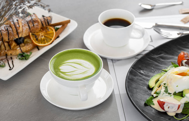 Xícara de latte e café matcha. Foto de alta qualidade. Matcha, chá verde latte em uma xícara e croissant. Fundo cinzento. Fecha. Vista superior. - Foto, Imagem