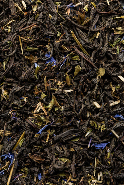 Heap of dry tea leaves. Dried black tea. Textured background of dried leaves of aromatic black tea with blue flowers. - Photo, Image