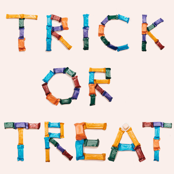 Halloween concept. Candies and chocolate bars arranged to create Trick or treat sign.  Flat lay. - Fotografie, Obrázek