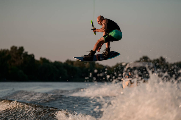 Athletic strong muscular man masterfully jumping on splashing wave on wakeboard - Zdjęcie, obraz